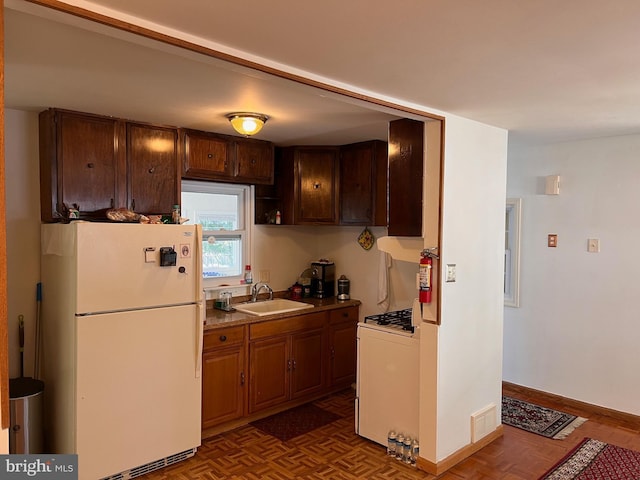 kitchen featuring visible vents, a sink, white appliances, light countertops, and baseboards