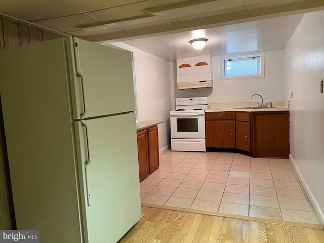 kitchen featuring white appliances, light wood-style flooring, a sink, light countertops, and under cabinet range hood