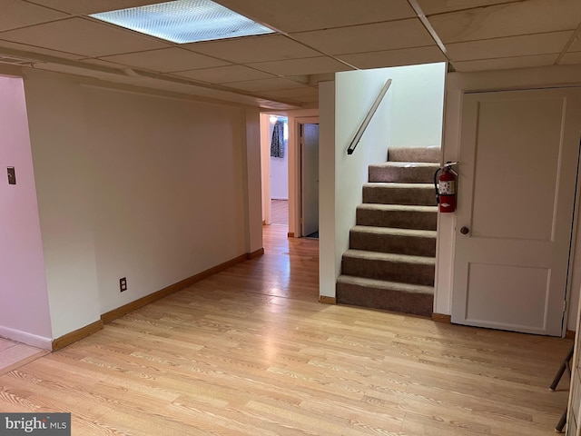 finished below grade area featuring a drop ceiling, light wood-type flooring, baseboards, and stairs