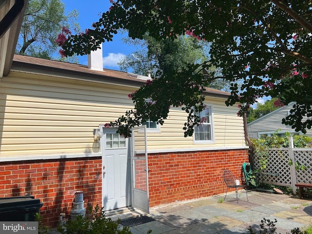 view of property exterior with a patio area, a chimney, and brick siding