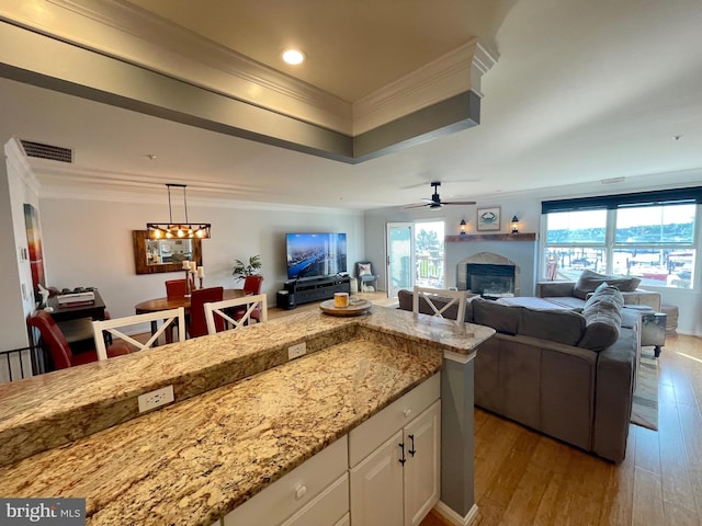 kitchen featuring ceiling fan, light stone counters, light hardwood / wood-style flooring, white cabinets, and ornamental molding