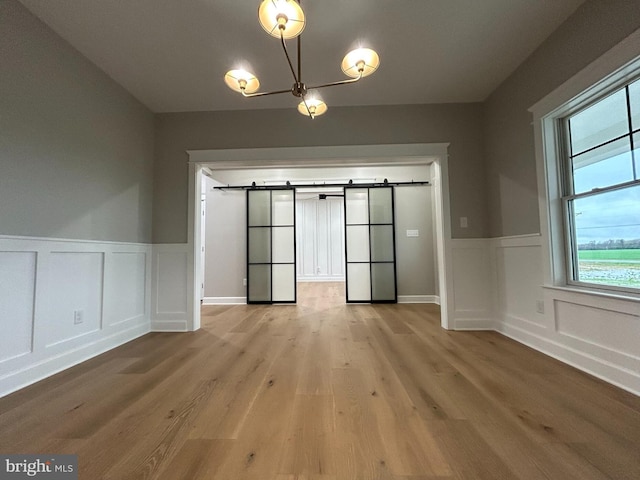 22430 Hummingbird Rd, Ellendale, DE 19941 - unfurnished dining area featuring a decorative wall, a barn door, wainscoting, and light wood-style floors