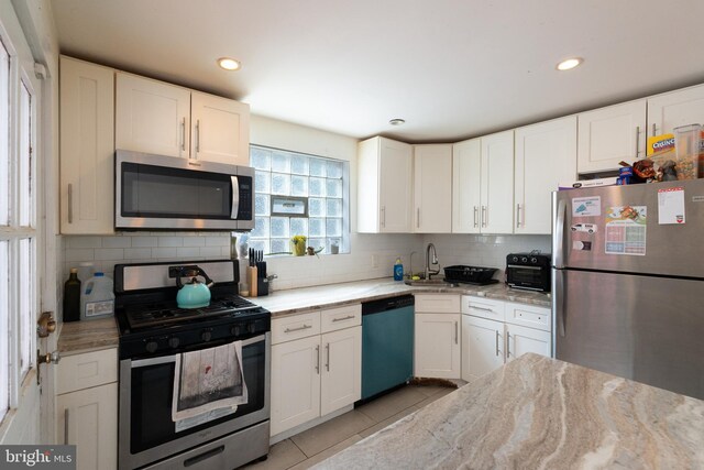 kitchen with light tile patterned floors, tasteful backsplash, white cabinets, stainless steel appliances, and a sink