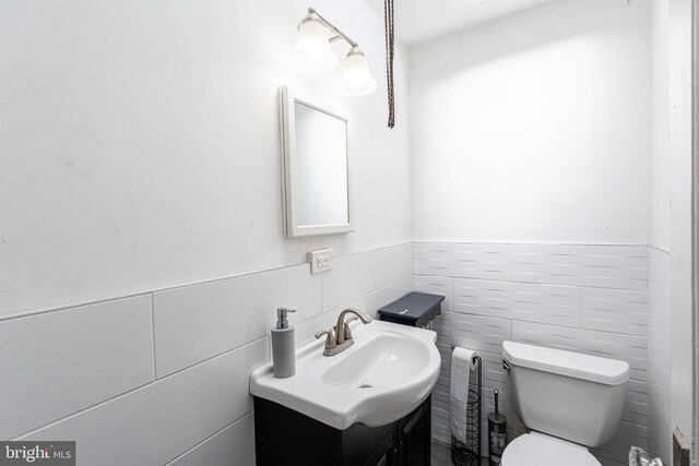 bathroom featuring toilet, a wainscoted wall, tile walls, and vanity