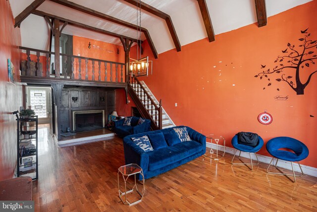 living area featuring a fireplace with raised hearth, wood finished floors, beamed ceiling, stairs, and high vaulted ceiling