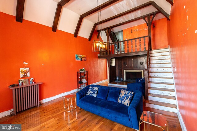 living area featuring lofted ceiling with beams, radiator heating unit, stairway, wood finished floors, and a fireplace