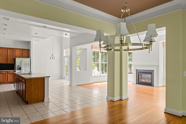 kitchen featuring stainless steel fridge, an island with sink, light wood-type flooring, decorative light fixtures, and ornamental molding