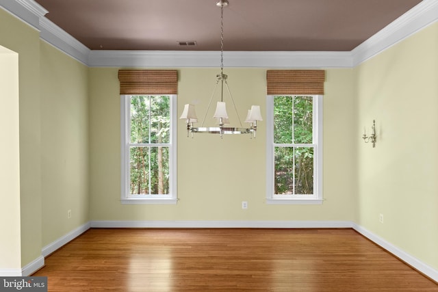 unfurnished dining area with a chandelier, ornamental molding, a healthy amount of sunlight, and hardwood / wood-style flooring