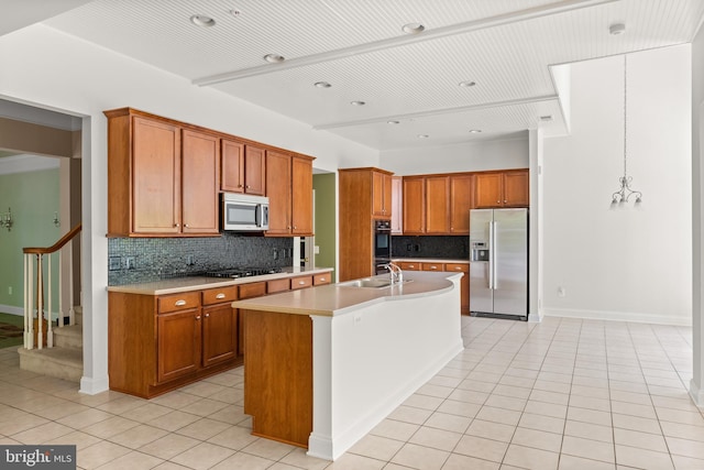 kitchen featuring pendant lighting, stainless steel appliances, tasteful backsplash, and an island with sink