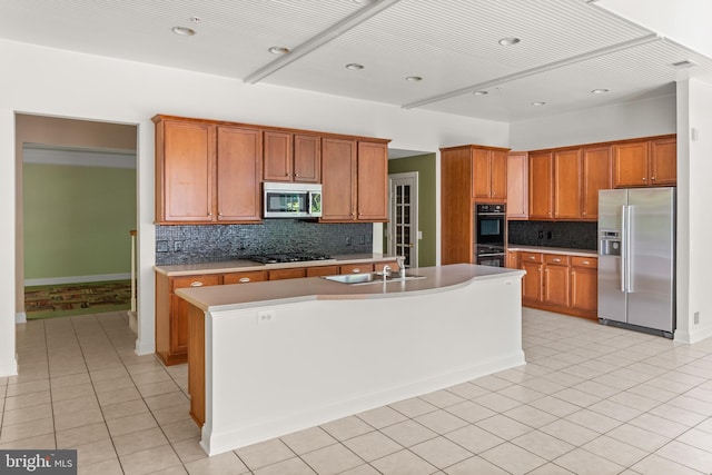 kitchen with sink, decorative backsplash, a center island with sink, light tile patterned floors, and appliances with stainless steel finishes