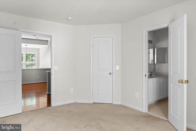 unfurnished bedroom featuring light colored carpet, ensuite bath, and sink