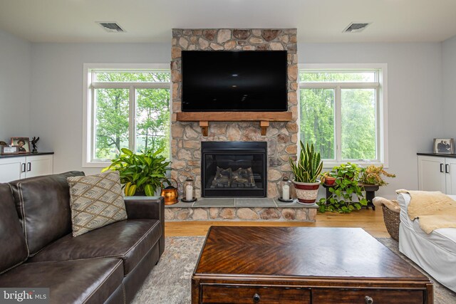 living room with a wealth of natural light, a stone fireplace, and light hardwood / wood-style floors