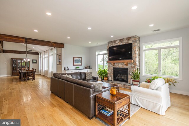 living room featuring beam ceiling, light hardwood / wood-style flooring, and a stone fireplace