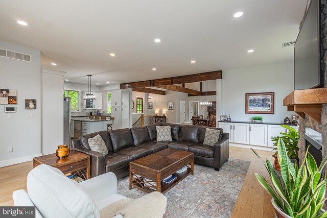 living room featuring light hardwood / wood-style floors, a stone fireplace, and beamed ceiling