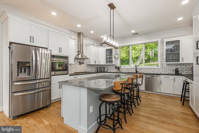 kitchen with stainless steel appliances, wall chimney exhaust hood, white cabinets, and a kitchen island