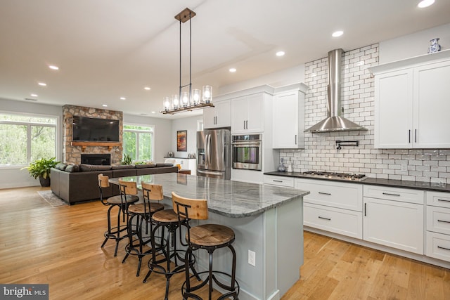 kitchen with a center island, white cabinetry, appliances with stainless steel finishes, a kitchen breakfast bar, and wall chimney exhaust hood