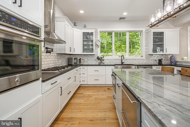 kitchen featuring stainless steel appliances, white cabinets, dark stone counters, and wall chimney range hood