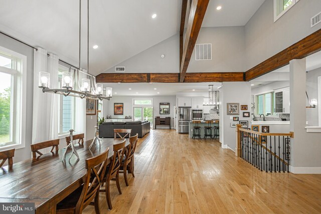 dining area featuring light wood-type flooring, beam ceiling, and a towering ceiling