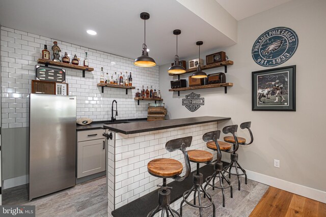 bar featuring tasteful backsplash, light hardwood / wood-style floors, sink, hanging light fixtures, and stainless steel refrigerator