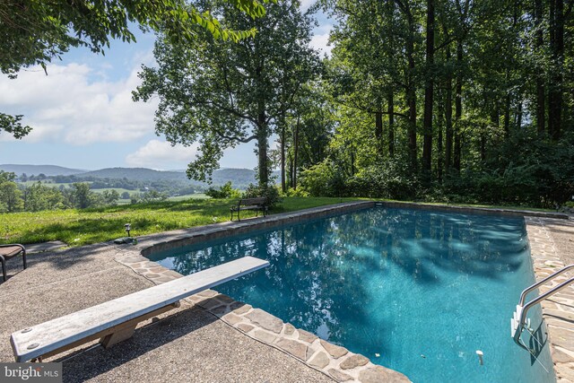 view of swimming pool with a diving board, a patio area, and a mountain view