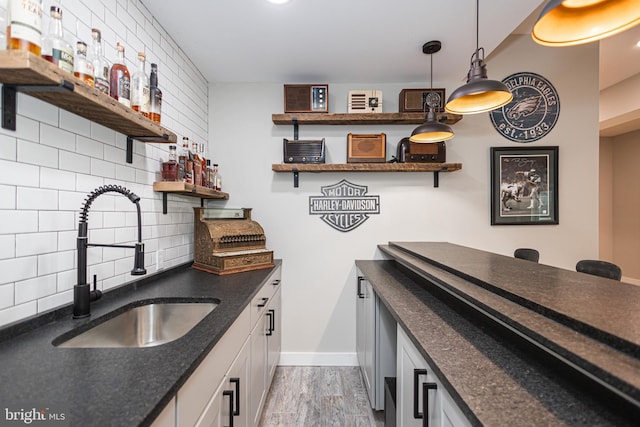 bar with tasteful backsplash, hardwood / wood-style floors, sink, hanging light fixtures, and white cabinets