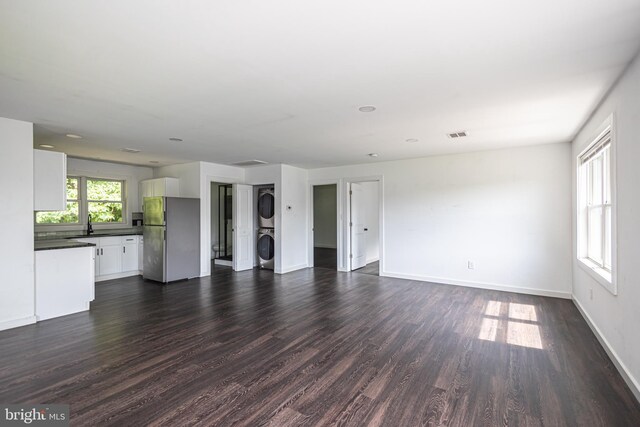 unfurnished living room featuring sink, stacked washer / drying machine, and dark hardwood / wood-style flooring