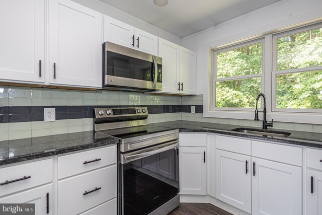 kitchen with white cabinetry, stainless steel appliances, dark hardwood / wood-style flooring, dark stone counters, and sink