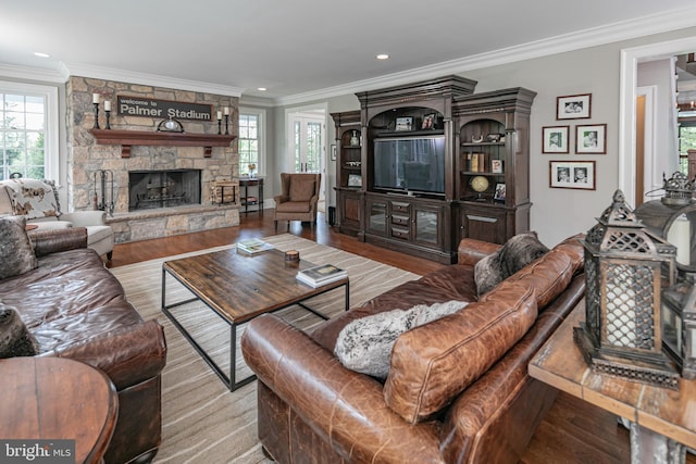 living room featuring hardwood / wood-style flooring, a stone fireplace, and crown molding