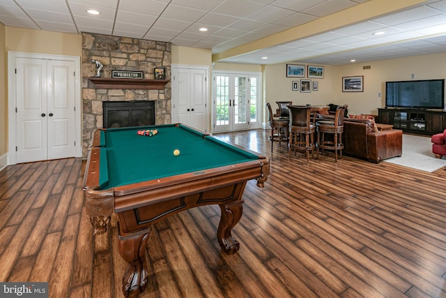 rec room with a stone fireplace, billiards, a drop ceiling, dark hardwood / wood-style floors, and french doors