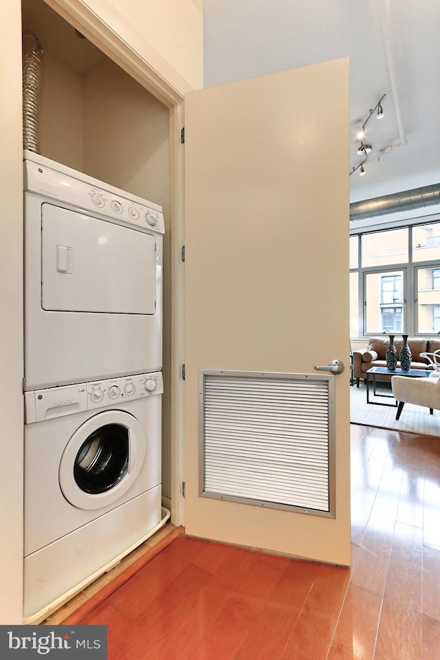 washroom with stacked washing maching and dryer, hardwood / wood-style flooring, and track lighting