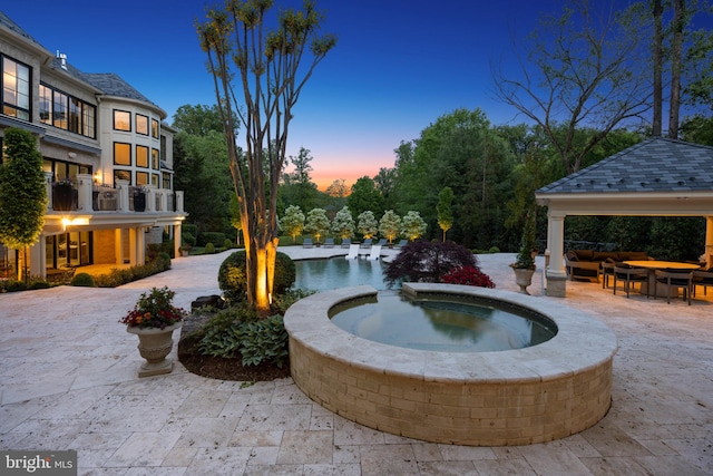 pool at dusk with a patio, an in ground hot tub, and a gazebo