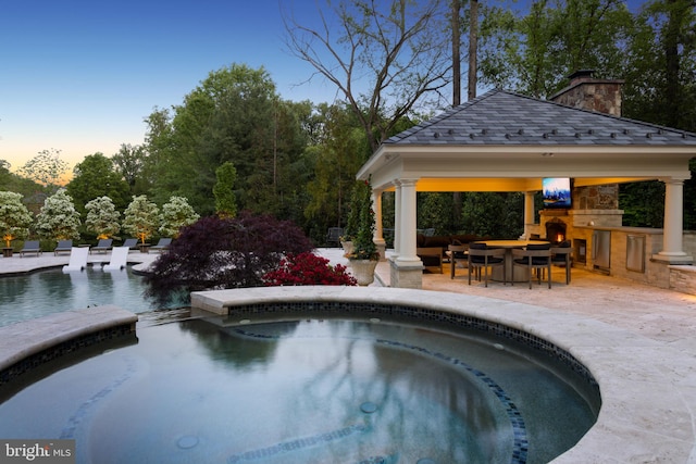 pool at dusk with a patio, exterior bar, an in ground hot tub, and a gazebo