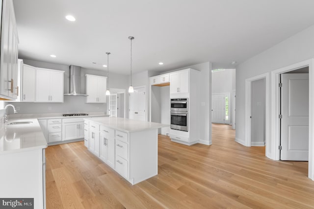 kitchen featuring stainless steel double oven, white cabinets, a center island, wall chimney exhaust hood, and sink