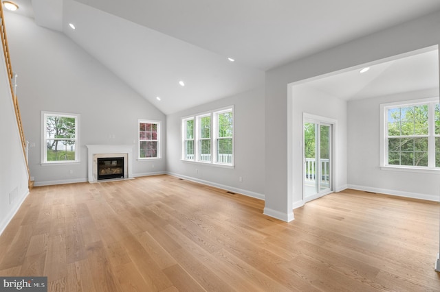 unfurnished living room with light hardwood / wood-style flooring, high vaulted ceiling, and a premium fireplace