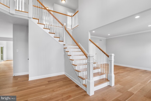 stairs featuring crown molding, hardwood / wood-style flooring, and a towering ceiling