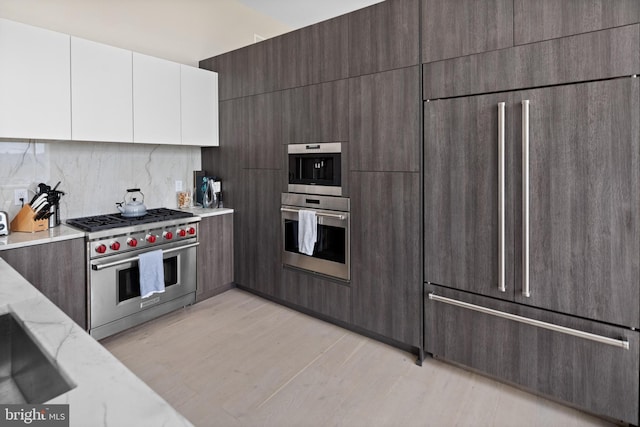 kitchen with tasteful backsplash, white cabinets, light hardwood / wood-style floors, light stone countertops, and premium appliances