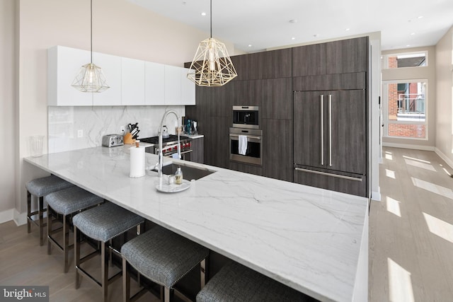 kitchen with tasteful backsplash, white cabinets, pendant lighting, dark brown cabinetry, and premium appliances