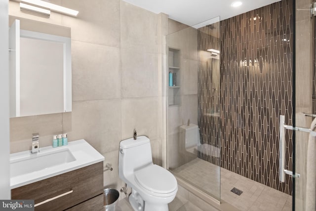 bathroom featuring tile walls, a shower with door, toilet, and vanity