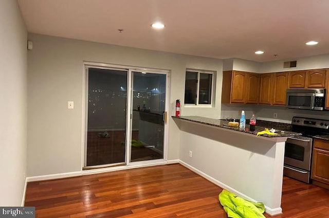 kitchen with dark stone countertops, stainless steel appliances, and dark wood-type flooring