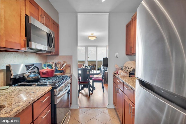 kitchen with a water view, stainless steel appliances, light stone countertops, and light tile floors