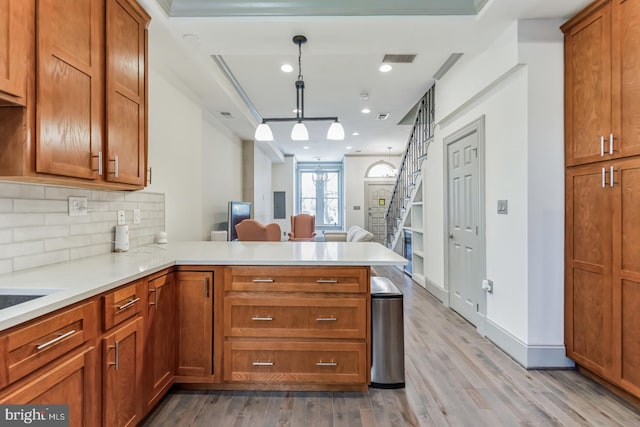 kitchen with decorative light fixtures, backsplash, kitchen peninsula, and light wood-type flooring