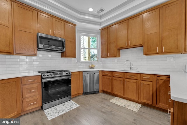 kitchen featuring appliances with stainless steel finishes, sink, backsplash, light wood-type flooring, and crown molding