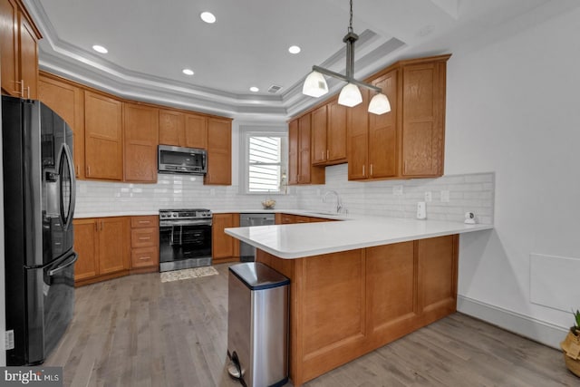 kitchen featuring hanging light fixtures, light hardwood / wood-style flooring, kitchen peninsula, stainless steel appliances, and a raised ceiling