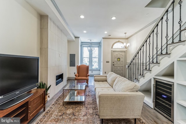 living room with a fireplace, wine cooler, a notable chandelier, ornamental molding, and hardwood / wood-style flooring