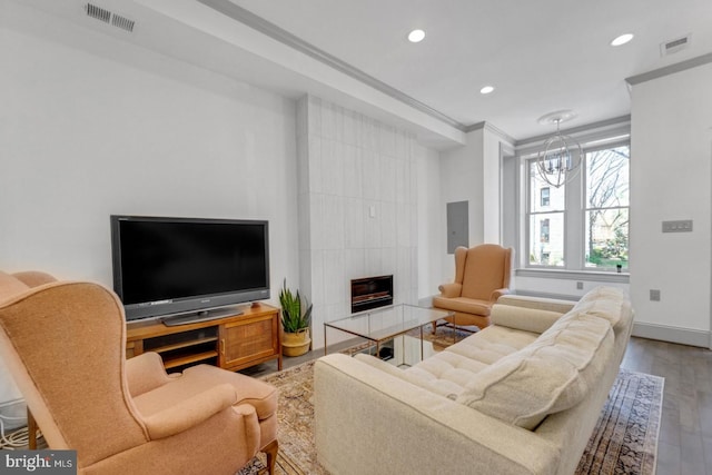 living room featuring wood-type flooring, crown molding, a tiled fireplace, and a chandelier