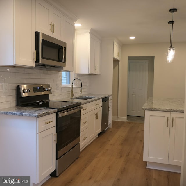 kitchen featuring white cabinetry, sink, stainless steel appliances, decorative light fixtures, and light wood-type flooring