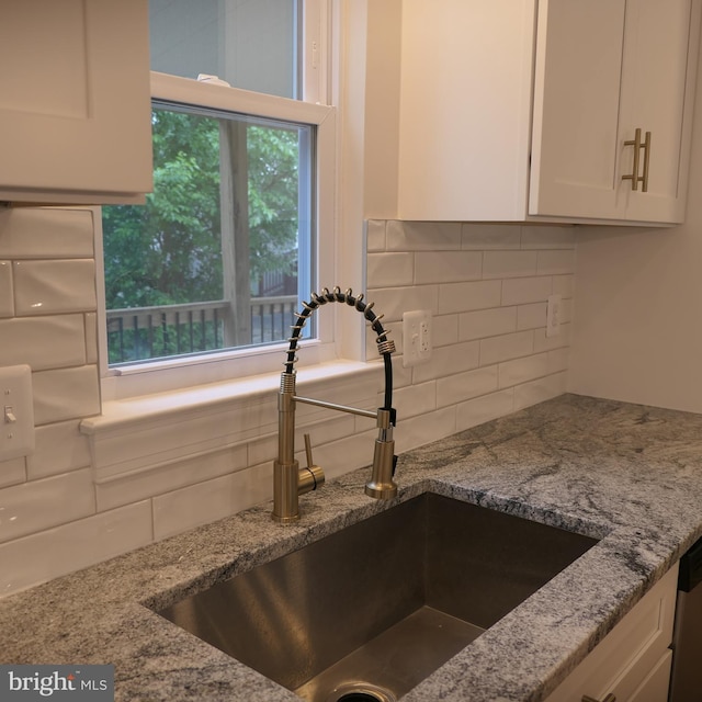 room details with white cabinets, light stone counters, sink, and backsplash