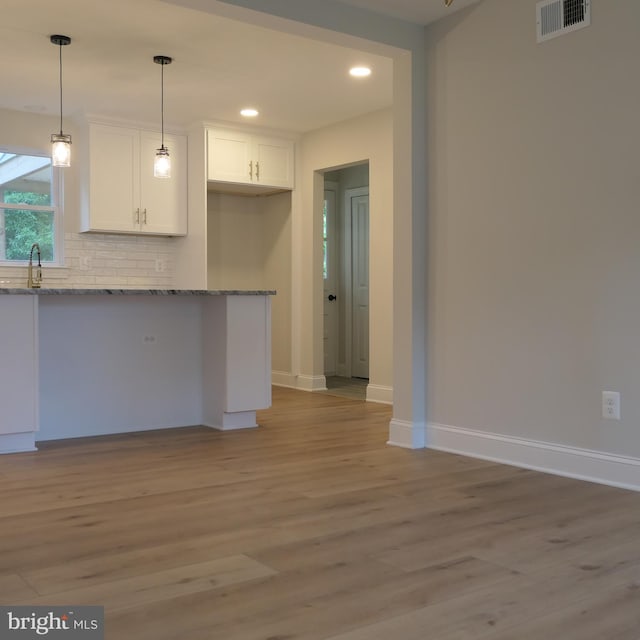 kitchen with light stone countertops, tasteful backsplash, pendant lighting, light hardwood / wood-style floors, and white cabinets