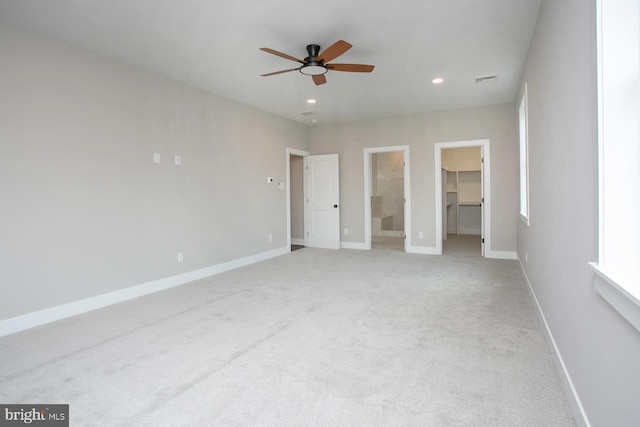 unfurnished bedroom featuring light colored carpet, ceiling fan, a spacious closet, connected bathroom, and a closet