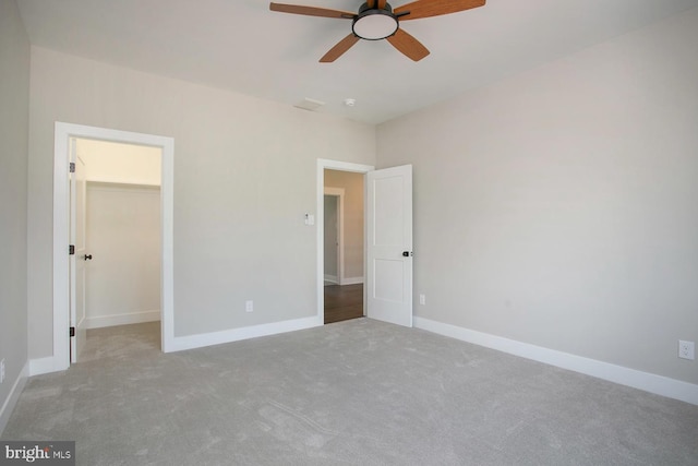 unfurnished bedroom featuring a spacious closet, a closet, ceiling fan, and light colored carpet